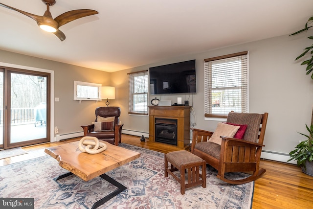 living room with baseboard heating, ceiling fan, and light hardwood / wood-style floors