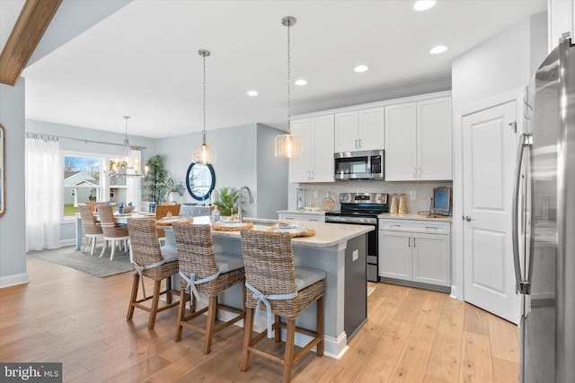 kitchen featuring a breakfast bar area, pendant lighting, stainless steel appliances, a kitchen island with sink, and white cabinets