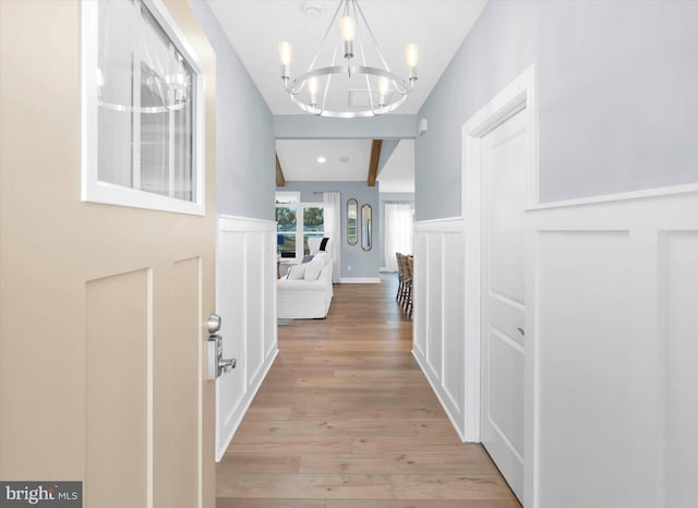 hallway with lofted ceiling, a notable chandelier, and light wood-type flooring