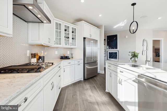 kitchen featuring wall chimney exhaust hood, sink, white cabinetry, decorative light fixtures, and stainless steel appliances