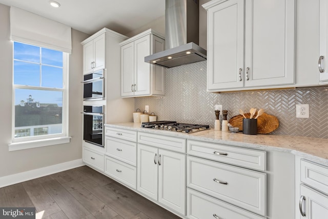 kitchen featuring wall chimney range hood, light stone countertops, dark hardwood / wood-style floors, and white cabinets