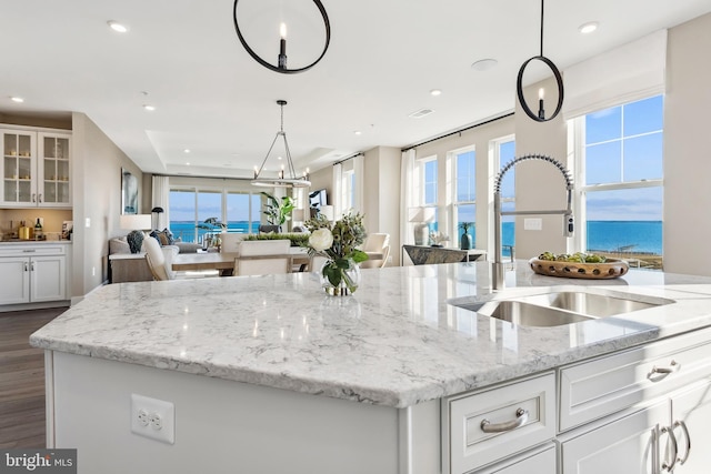 kitchen featuring white cabinetry, sink, decorative light fixtures, and a water view