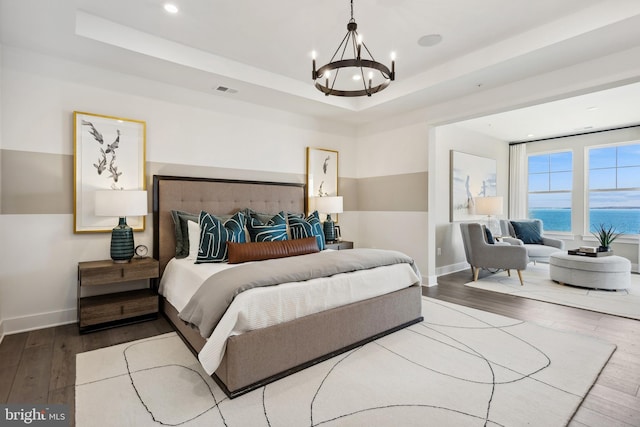 bedroom featuring a tray ceiling, hardwood / wood-style flooring, a chandelier, and a water view