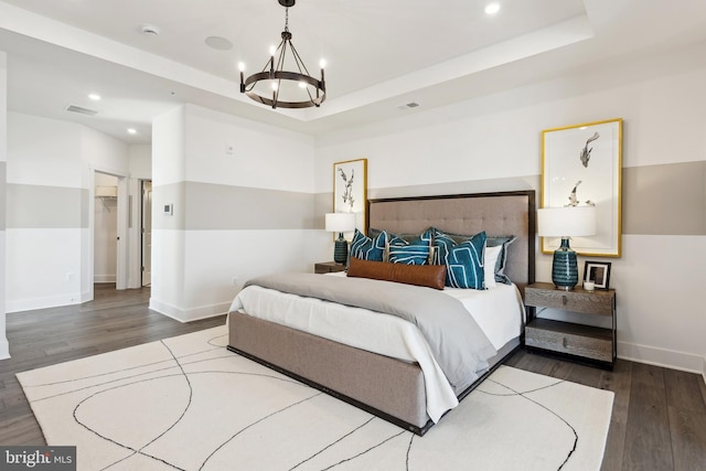 bedroom with a walk in closet, wood-type flooring, a raised ceiling, and a chandelier