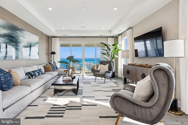 living room featuring a tray ceiling, light wood-type flooring, and a wealth of natural light