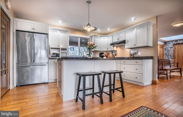 kitchen with under cabinet range hood, white cabinetry, a kitchen breakfast bar, high end fridge, and pendant lighting