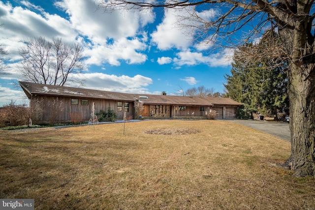 ranch-style house featuring a front yard, driveway, a chimney, and an attached garage