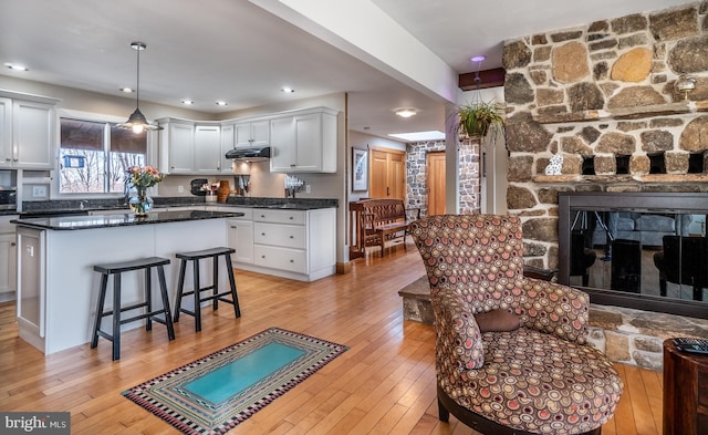 living room featuring a stone fireplace, recessed lighting, and light wood-style floors