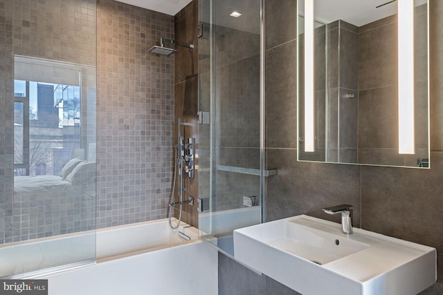 bathroom featuring tile walls, sink, and enclosed tub / shower combo