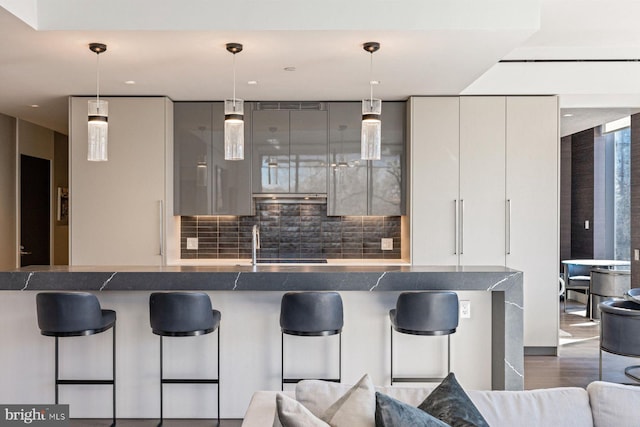 kitchen featuring decorative light fixtures, dark hardwood / wood-style floors, decorative backsplash, and a kitchen bar