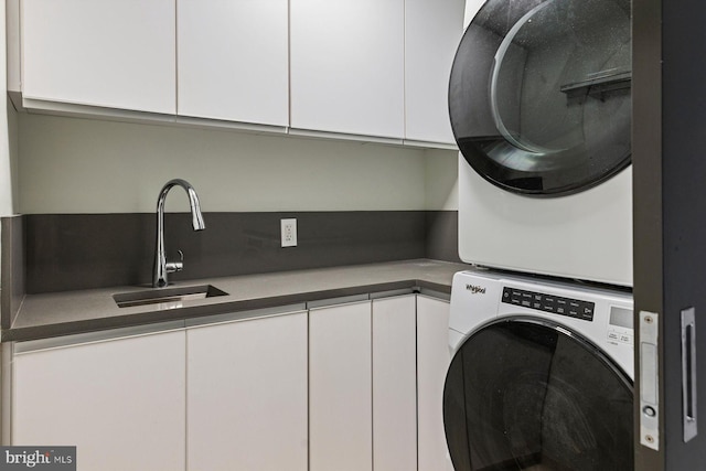 laundry area featuring cabinets, stacked washer / dryer, and sink