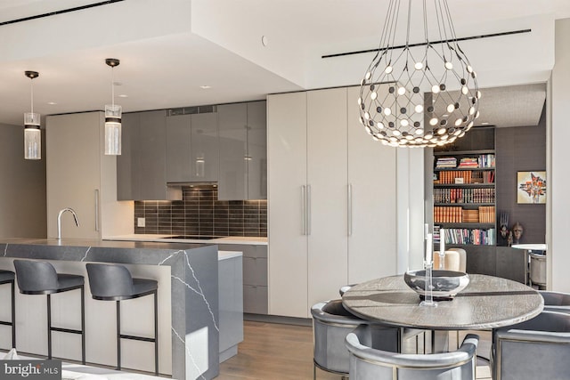 kitchen featuring gray cabinetry, tasteful backsplash, a notable chandelier, pendant lighting, and light hardwood / wood-style floors