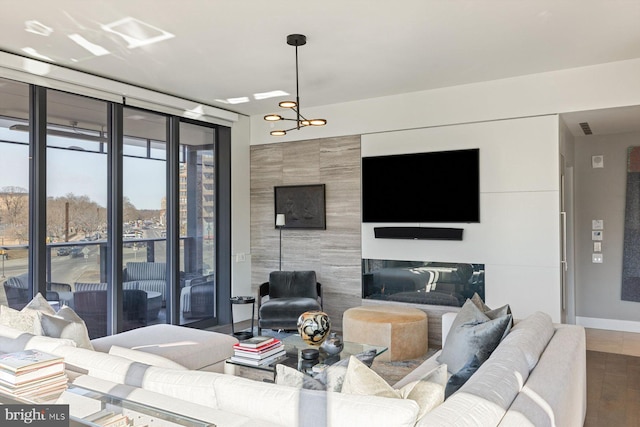 living room with a tiled fireplace, hardwood / wood-style floors, a wall of windows, and an inviting chandelier