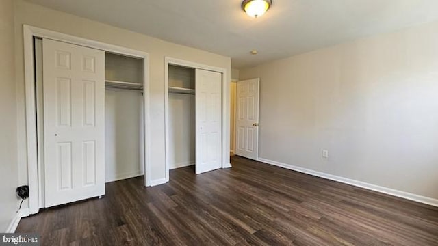 unfurnished bedroom with multiple closets and dark hardwood / wood-style floors