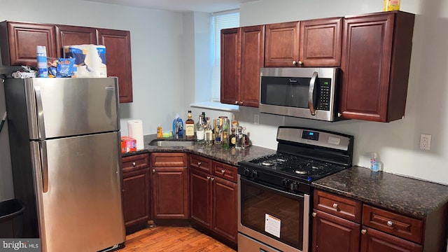 kitchen with appliances with stainless steel finishes, sink, dark stone countertops, and light hardwood / wood-style floors