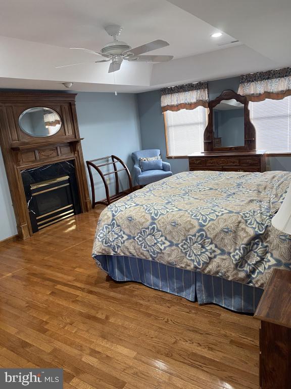 bedroom featuring hardwood / wood-style floors, a tray ceiling, a fireplace, and ceiling fan