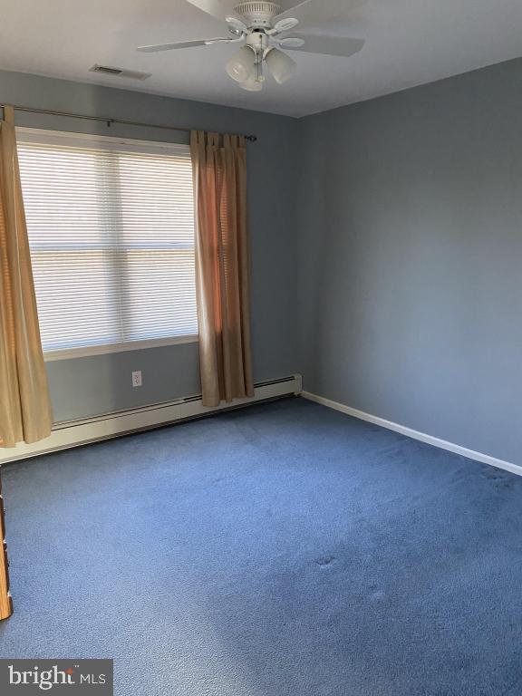 spare room featuring dark colored carpet, ceiling fan, and a baseboard heating unit