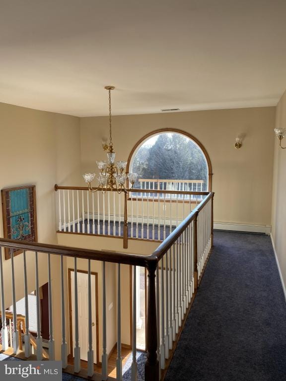 hallway with an inviting chandelier, dark carpet, a baseboard radiator, and a towering ceiling