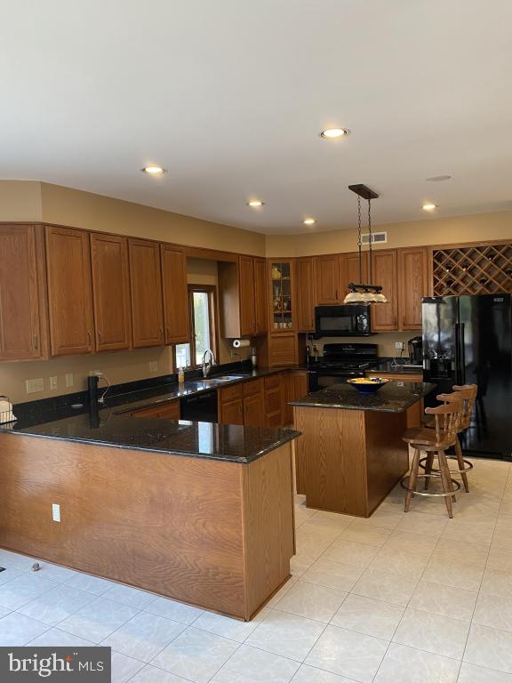 kitchen featuring a center island, hanging light fixtures, a kitchen breakfast bar, dark stone counters, and black appliances