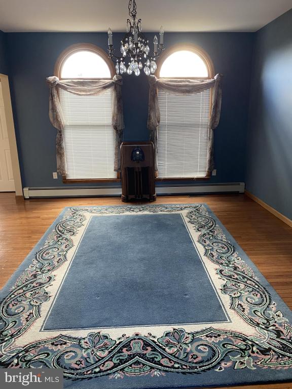 unfurnished dining area with wood-type flooring, an inviting chandelier, and baseboard heating