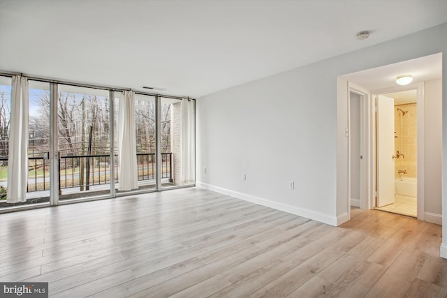 spare room with a wall of windows and light hardwood / wood-style floors