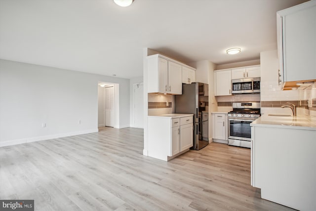 kitchen featuring sink, white cabinetry, appliances with stainless steel finishes, light hardwood / wood-style floors, and backsplash