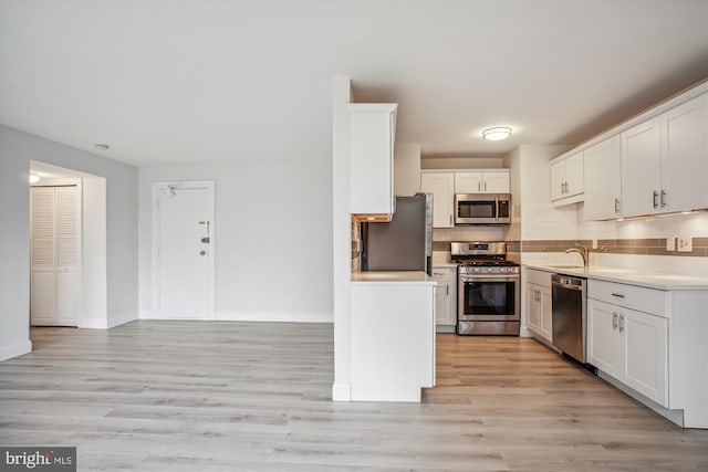 kitchen with sink, white cabinetry, stainless steel appliances, decorative backsplash, and light wood-type flooring