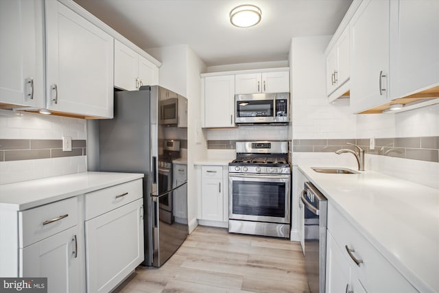 kitchen with sink, white cabinetry, light wood-type flooring, stainless steel appliances, and decorative backsplash