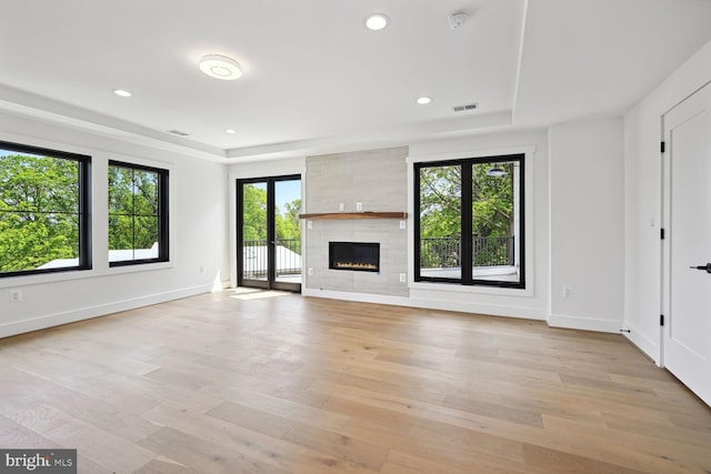 unfurnished living room featuring light wood-style flooring, a raised ceiling, visible vents, and baseboards