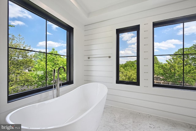 full bath featuring marble finish floor, a freestanding bath, and wooden walls