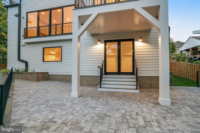 back of property at dusk featuring entry steps, a patio area, fence, and a balcony