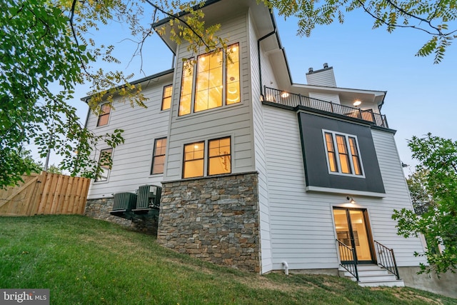 back of property featuring a yard, central AC unit, entry steps, fence, and a balcony