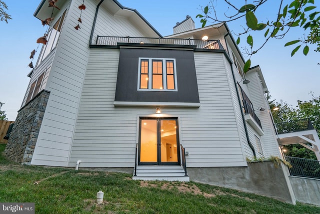 view of front facade with a chimney, entry steps, a front yard, fence, and a balcony