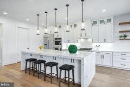 kitchen featuring decorative light fixtures, white cabinetry, light countertops, a kitchen bar, and glass insert cabinets