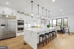 kitchen featuring an island with sink, appliances with stainless steel finishes, decorative light fixtures, light countertops, and white cabinetry