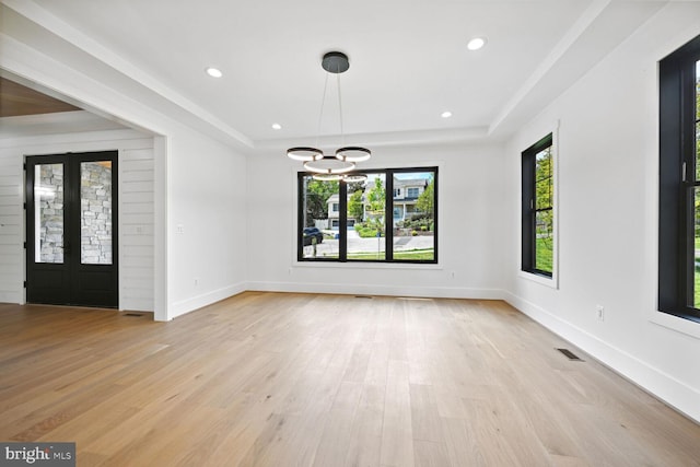 interior space with a tray ceiling, light wood-type flooring, and visible vents