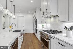 kitchen featuring white cabinetry, high end stainless steel range oven, hanging light fixtures, and light stone countertops