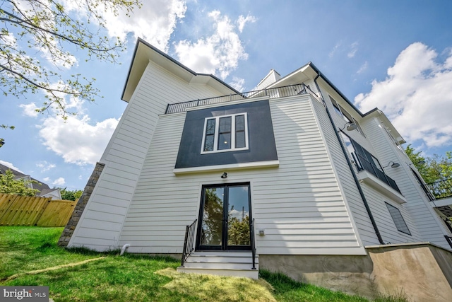 rear view of house with entry steps, a lawn, fence, and a balcony