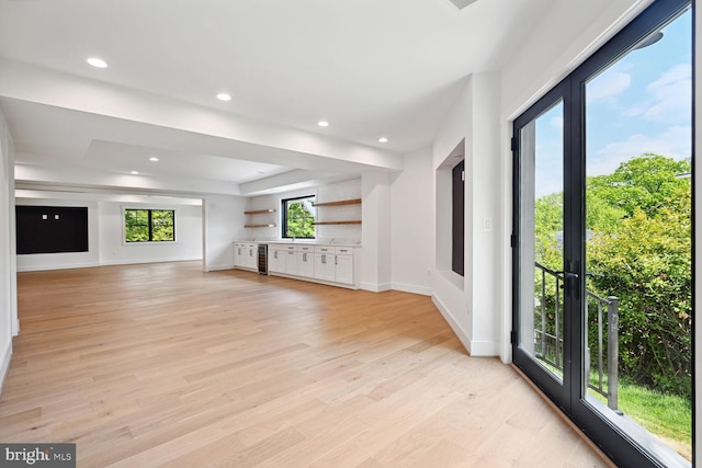 unfurnished living room with light wood-type flooring, a tray ceiling, baseboards, and recessed lighting