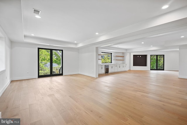 unfurnished living room featuring plenty of natural light, a raised ceiling, visible vents, and light wood-style floors