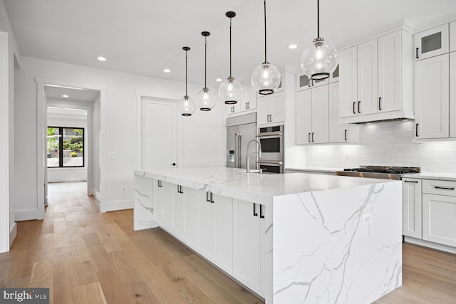 kitchen featuring decorative light fixtures, glass insert cabinets, a large island with sink, and white cabinets