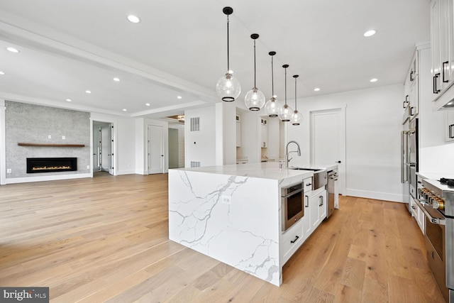 kitchen featuring light stone counters, white cabinetry, open floor plan, a large island, and pendant lighting