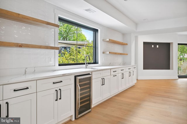 kitchen featuring white cabinets, wine cooler, light stone countertops, open shelves, and a sink