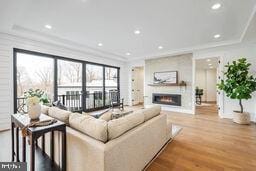 living room with a warm lit fireplace, recessed lighting, wood finished floors, and crown molding