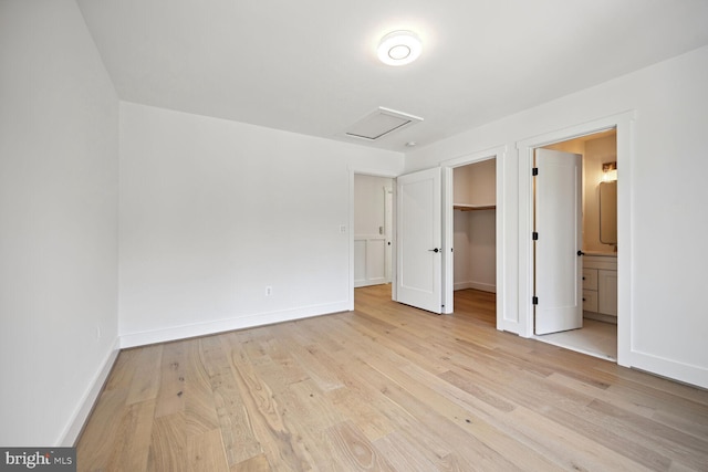 unfurnished bedroom with baseboards, light wood-style floors, a spacious closet, a closet, and attic access