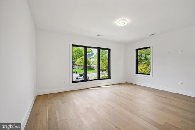 unfurnished room featuring light wood-style floors, baseboards, visible vents, and a wealth of natural light