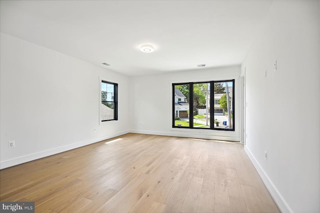 spare room featuring baseboards, a wealth of natural light, and light wood-style floors