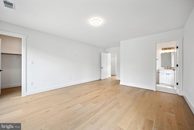 unfurnished bedroom with visible vents, baseboards, light wood-style flooring, ensuite bathroom, and a spacious closet