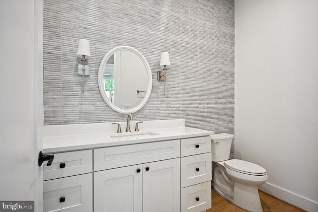 half bathroom with toilet, wood finished floors, vanity, and baseboards