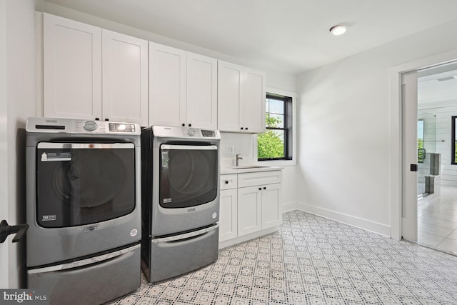 clothes washing area featuring light floors, cabinet space, washing machine and dryer, a sink, and baseboards